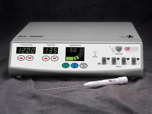Generador de corriente alterna RF 3000 y electrodo tipo LeVeen, con las púas o electrodos secundarios desplegados. En la cara frontal del generador pueden observarse las ventanas para monitorizar el tiempo aplicado (izquierda), la potencia de la corriente aplicada (centro) y la impedancia tisular registrada (derecha), así como los interruptores para comenzar y finalizar el paso de corriente. En el lado derecho, las conexiones con el electrodo principal y las 4 placas de retorno.
