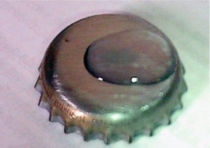 Tampinha de garrafa com a solução de Gota Salina colocada sobre a superfície metálica.