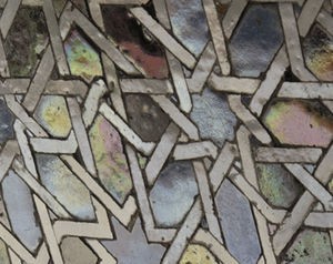 Fotografía de una zona en la que predominan azulejos de tonos negros en los que se pueden observar cambios de tono (efectos iridiscentes) así como apariencia metalizada y de metal líquido.