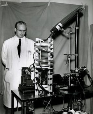 Richard De Wall junto al oxigenador de burbujas De Wall-Lillehei. Richard De Wall junto al oxigenador de burbujas De Wall-Lillehei, compuesto del tubo intercambiador de oxígeno (a la derecha), el recipiente para desburbujear (sobre éste) y el reservorio de hélice (a la izquierda), con el que 13 de mayo de 1955 Lillehei corrigió una Tetralogía de Fallot en un lactante de 22 meses. Cortesía de University of Minnesota.
